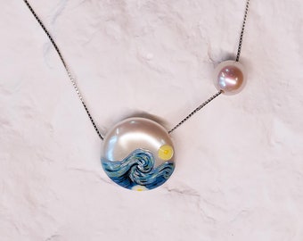 May include: A silver chain necklace with a pearl pendant featuring a painted image of a wave and a yellow sun. A second pearl pendant hangs from the chain.