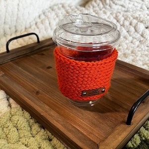 May include: Orange crocheted coffee cup cozy with a brown leather tag that says "Handmade by Sarah".