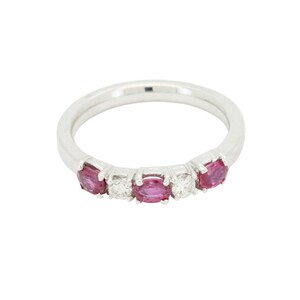 May include: A silver ring with five gemstones. The ring features three oval-cut, deep pink gemstones and two smaller, round, clear gemstones. The ring is set against a white background.