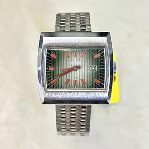 Puede incluir: Reloj de pulsera plateado vintage con esfera rectangular y correa metálica a juego. La esfera tiene un fondo verde a rayas con marcadores y agujas rojas, y una pantalla de fecha. Un accesorio clásico.