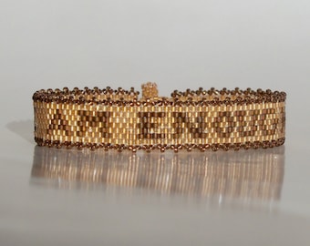 May include: A brown and gold beaded bracelet with a geometric pattern.