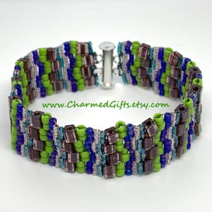 May include: A beaded bracelet with a silver clasp. The bracelet features a pattern of green, blue, and brown beads. The text "www.CharmedGifts.etsy.com" is visible on the image.