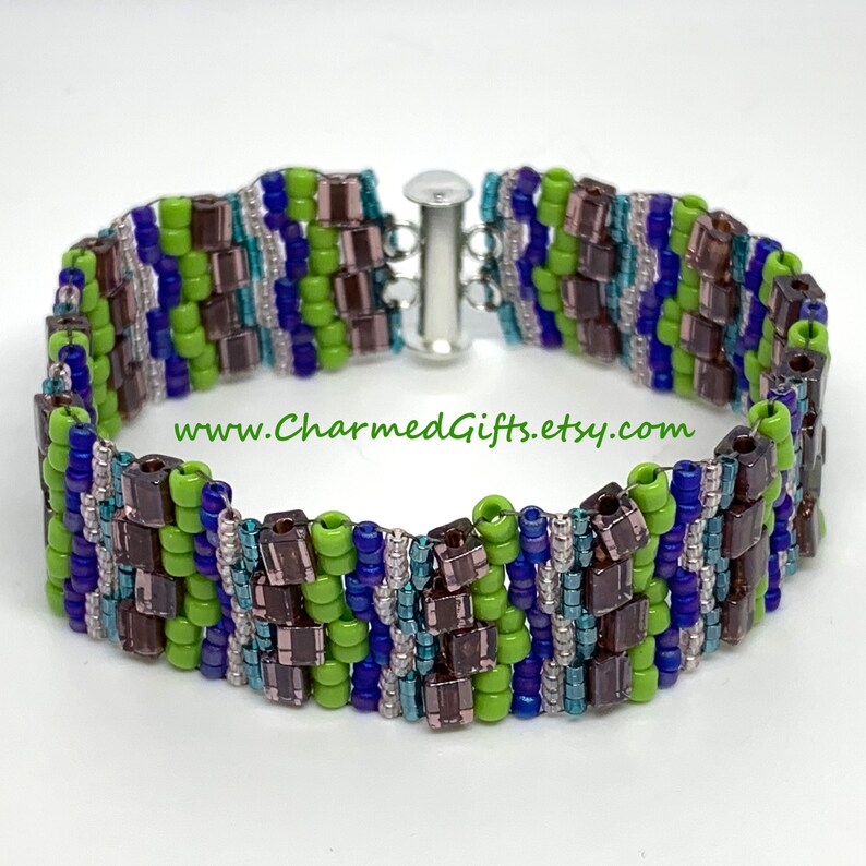 May include: A beaded bracelet with a silver clasp. The bracelet features a pattern of green, blue, and brown beads. The text "www.CharmedGifts.etsy.com" is visible on the image.