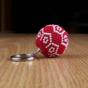May include: A red and white beaded keychain with a geometric pattern. The keychain is attached to a silver key ring.