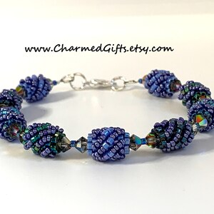 Könnte beinhalten: Ein Armband mit Perlen und einem silbernen Verschluss zeigt ein sich wiederholendes Muster aus blauen und violetten Spiralperlen, die mit klaren Kristallperlen durchsetzt sind.