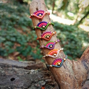 Pode incluir: Uma pilha de seis pulseiras tecidas com padrões de fios coloridos em forma de leque, cada uma acentuada com uma pequena conta metálica no centro. As pulseiras estão dispostas verticalmente, exibindo várias combinações de cores, incluindo rosa, verde, laranja e azul.