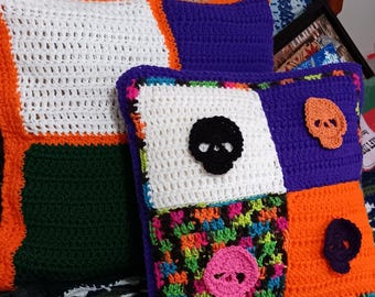 May include: Crocheted decorative pillows with a patchwork design. One pillow features a white square with a black skull, and another has a pink skull. The pillows have orange, purple, green, and white squares.
