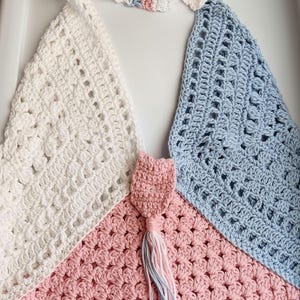 May include: A crocheted bag with a white, pink, and blue color scheme. The bag has a triangular shape and a tassel.