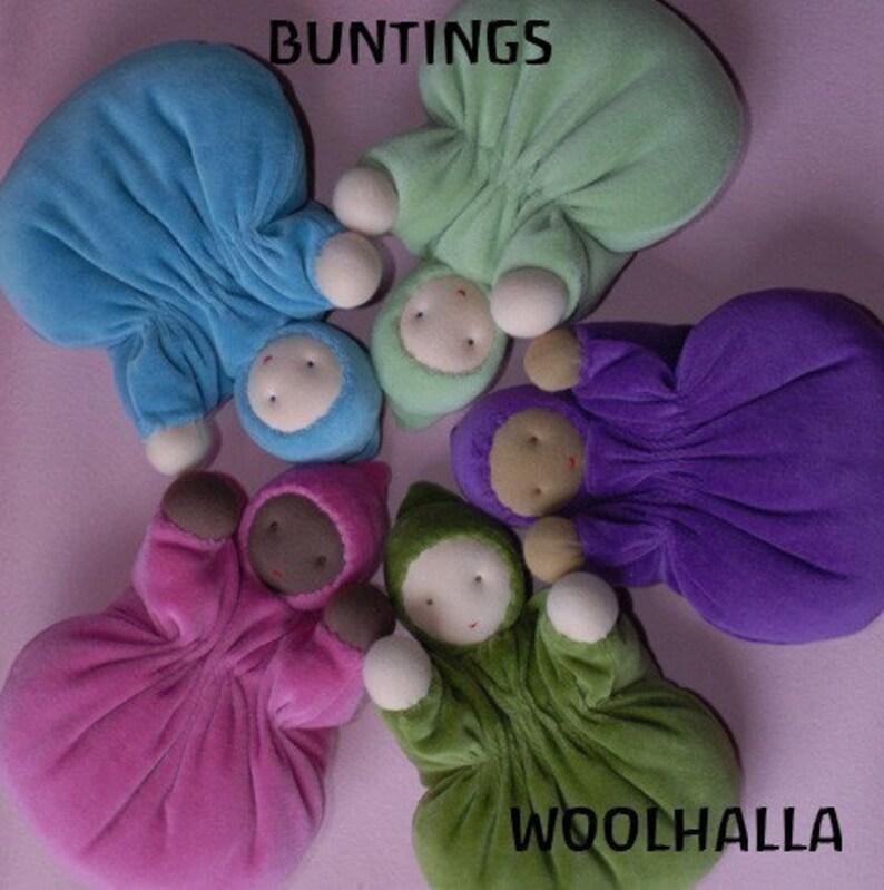 Pu&ograve; includere: Una collezione di bambole per bambini in peluche colorate, in vari colori tra cui blu, verde, viola, rosa e verde. Ogni bambola ha un viso rotondo e un abito con cappuccio. Le parole "BUNTINGS" e "WOOLHALLA" sono visibili.