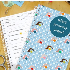 May include: A blue and white spiral bound notebook with a swimming themed cover. The cover features a pattern of swimmers and waves. The text "Katya's swimming journal" is printed on the cover.
