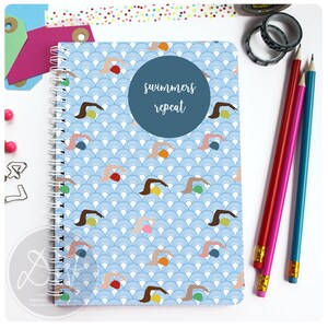 May include: A blue spiral notebook with a repeating pattern of swimmers and waves. The cover has a blue circle with the text "swimmers repeat" in white.