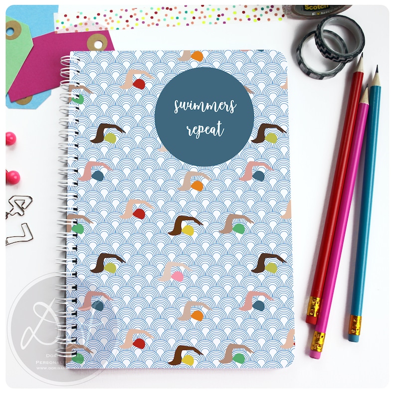 May include: A blue spiral notebook with a repeating pattern of swimmers and waves. The cover has a blue circle with the text "swimmers repeat" in white.