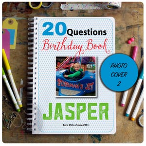 May include: A blue and white polka dot notebook with the text "20 Questions Birthday Book" in red and blue. The cover features a photo of a child on a blue ride with the text "Spiderman's Jet". The name "Jasper" is written in green letters below the photo. The text "Born 15th of June 2011" is written below the name.