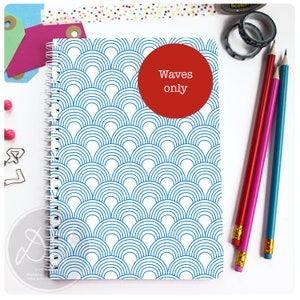 May include: A white spiral bound notebook with a blue and white wave pattern on the cover. A red circle with the text "Waves only" is on the front cover.