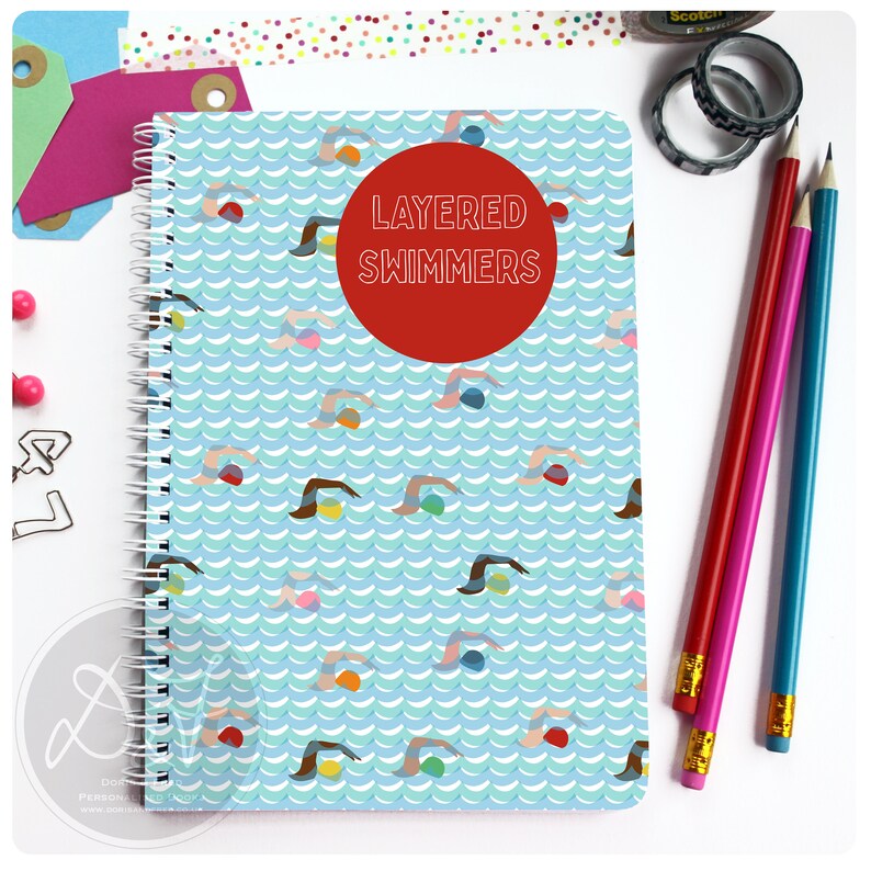 May include: A blue spiral notebook with a pattern of swimmers and waves. The cover has a red circle with the text "LAYERED SWIMMERS" in white.