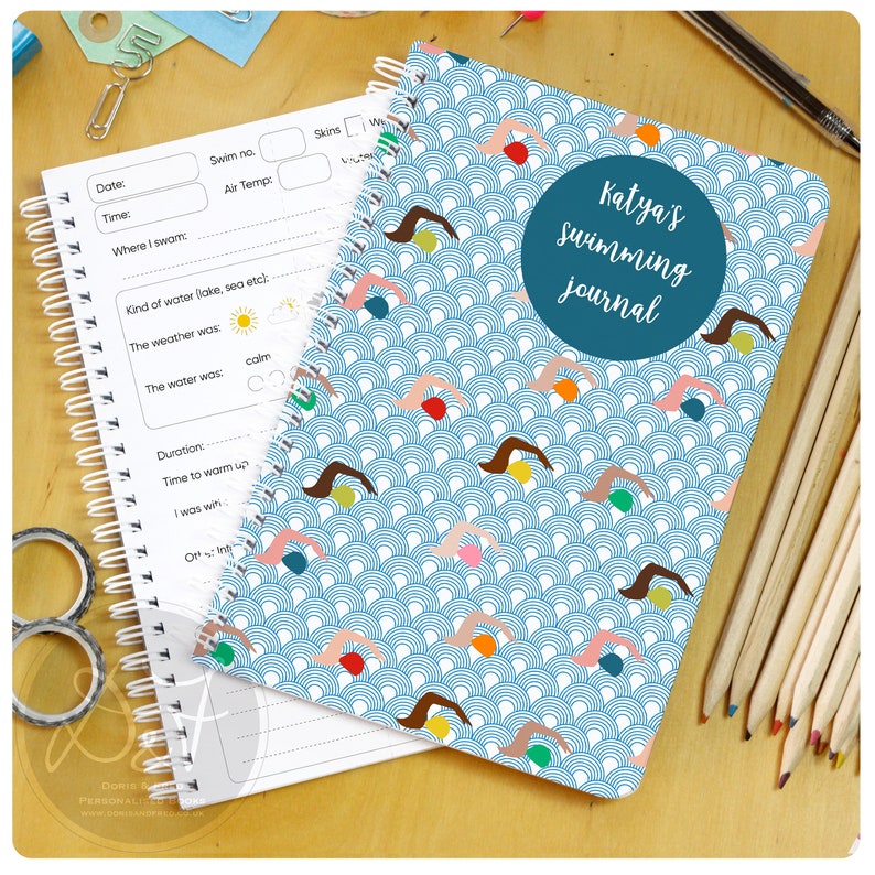 May include: A blue and white spiral bound notebook with a swimming themed cover. The cover features a pattern of swimmers and waves. The text "Katya's swimming journal" is printed on the cover.