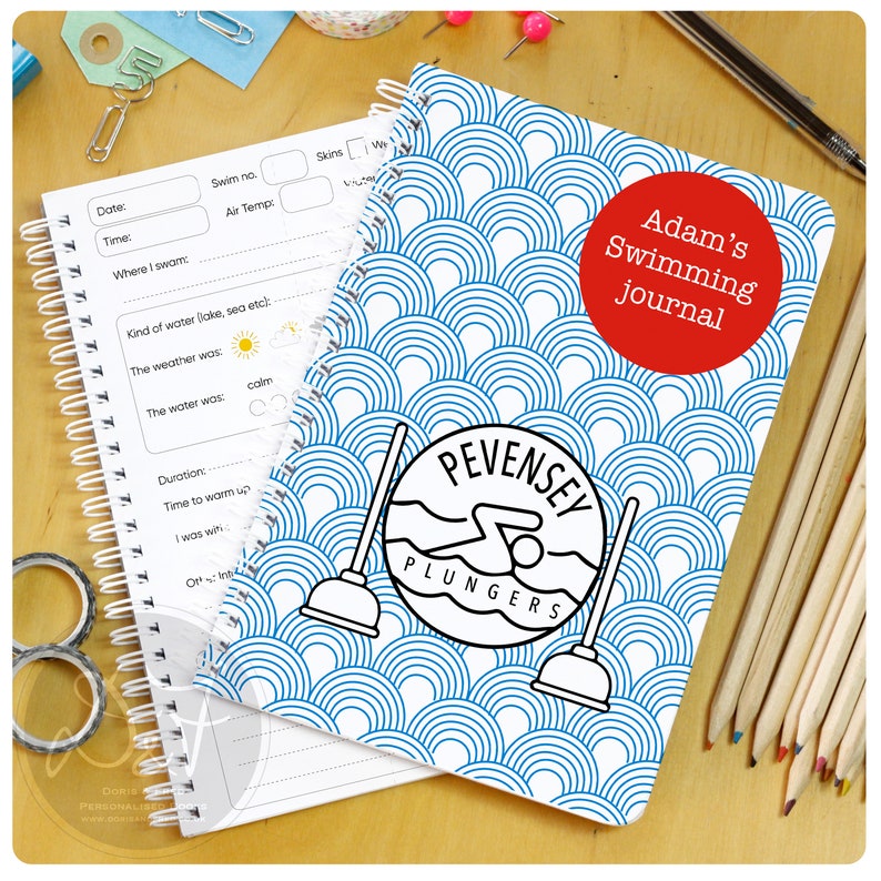 May include: A blue and white spiral bound notebook with a swimming themed cover. The cover features a swimmer in a circle with the text "Pevensey Plungers". The notebook also has the text "Adam's Swimming Journal" in a red circle.