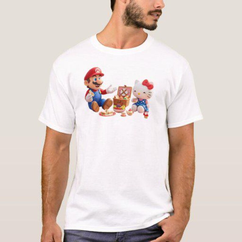 May include: White t-shirt featuring a colorful graphic of Mario and Hello Kitty having a picnic. Mario is wearing his signature red hat and blue overalls. Hello Kitty is in a blue dress with a red bow. A picnic basket and food are also visible.