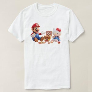 May include: White t-shirt featuring a colorful graphic of Mario and Hello Kitty having a picnic. Mario is wearing his signature red hat and blue overalls. Hello Kitty is in a blue dress with a red bow. A picnic basket and food are also visible.