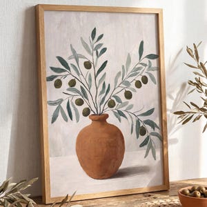 May include: A framed wall art print featuring a painting of a terracotta-coloured clay vase holding olive branches with green leaves and dark green olives. The artwork is set against a light, neutral background and enclosed in a light wood frame.