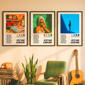 Puede incluir: Tres impresiones artísticas enmarcadas con bordes negros. Las impresiones presentan imágenes de estilo retro de un coche, una mujer y una persona sobre un fondo azul. Cada impresión incluye una lista de pistas, el nombre del artista y el nombre del álbum. Una guitarra, una silla y discos están en primer plano.