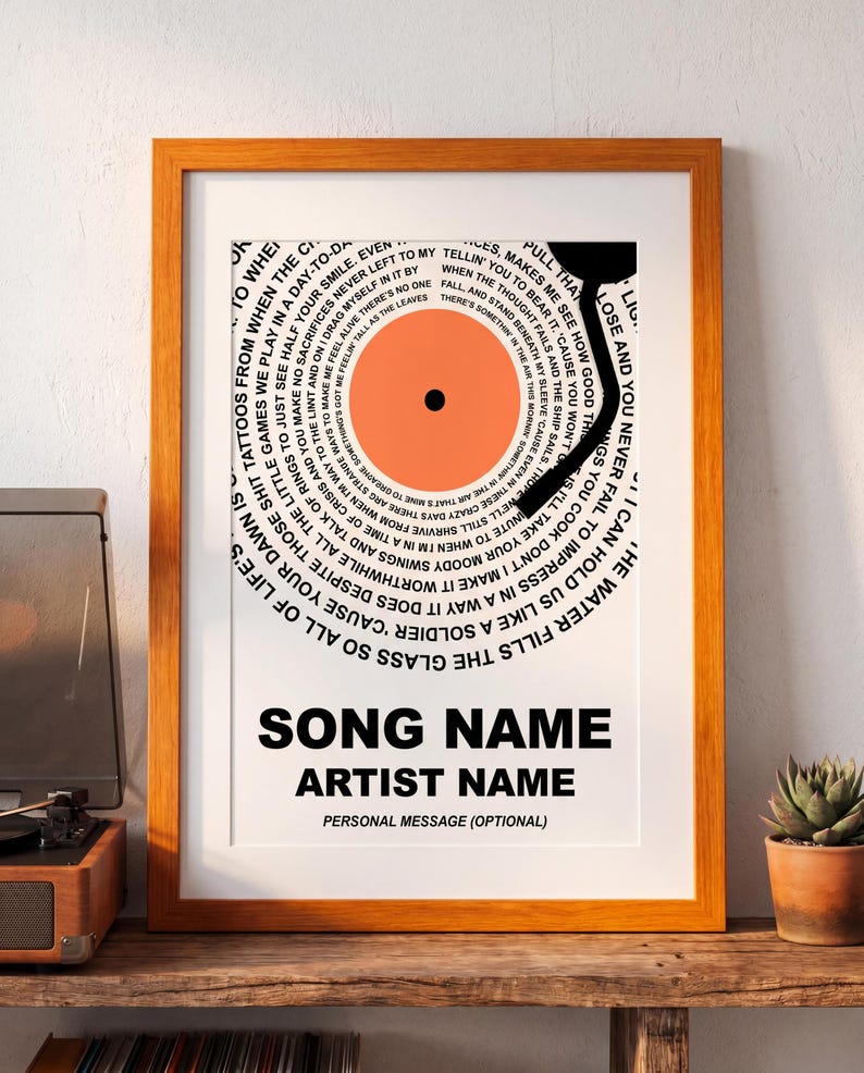 May include: Framed print featuring a vinyl record design with song lyrics circling the center. The record is orange with a black center and a black tonearm. The print includes space for song and artist names, and a personal message.