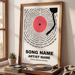 May include: A framed print featuring a vinyl record design with a red center and black arm. The design includes song lyrics in a circular pattern around the record. The text at the bottom reads "SONG NAME" and "ARTIST NAME".
