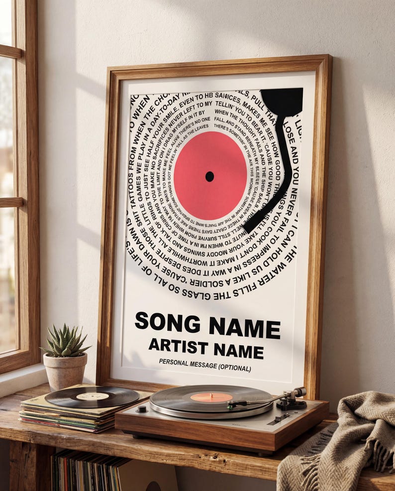 May include: A framed print featuring a vinyl record design with a red center and black arm. The design includes song lyrics in a circular pattern around the record. The text at the bottom reads "SONG NAME" and "ARTIST NAME".