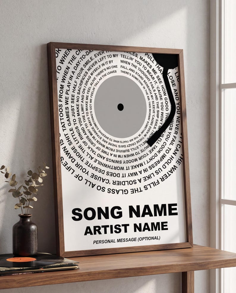 May include: A framed print featuring a stylized vinyl record design with song lyrics in a circular pattern. The print has a black and gray color scheme with the song name, artist name, and optional personal message at the bottom.