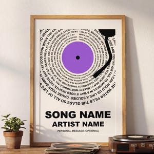 May include: A framed print featuring a stylized vinyl record design. The record is purple with a black center and surrounded by song lyrics in a circular pattern. The print includes the text "SONG NAME", "ARTIST NAME", and "PERSONAL MESSAGE (OPTIONAL)".