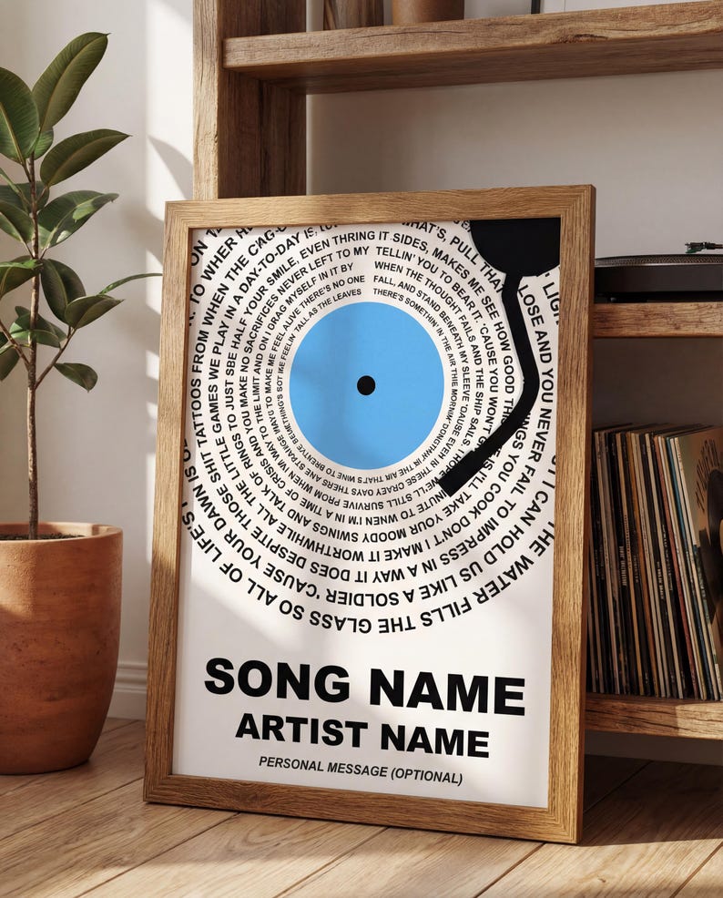 May include: Framed print featuring a blue vinyl record design with song lyrics and a wooden frame. The print includes space for a song name, artist name, and a personal message. The background is white.