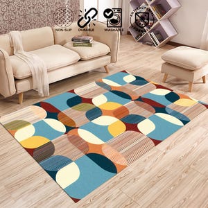 May include: A rectangular area rug with a geometric pattern of overlapping shapes in blue, yellow, orange, and brown. The rug is labeled as non-slip, durable, and washable. It is placed on a wooden floor.