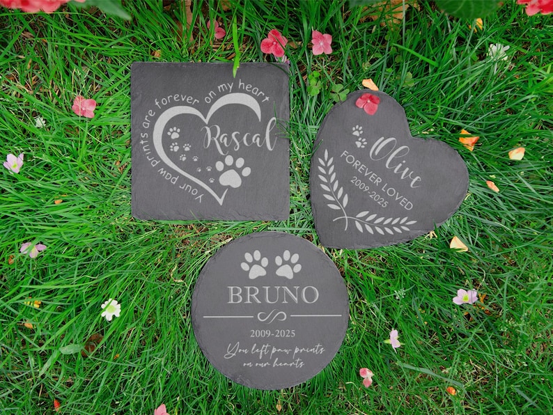 Puede incluir: Tres l&aacute;pidas conmemorativas para mascotas de pizarra gris oscuro en varias formas: cuadrada, coraz&oacute;n y c&iacute;rculo. Cada piedra est&aacute; grabada con el nombre de una mascota, huellas de patas y texto conmemorativo. Las piedras est&aacute;n sobre hierba verde con peque&ntilde;as flores rosas.