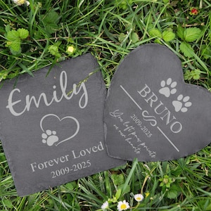 Puede incluir: Dos piedras conmemorativas para mascotas de pizarra. Una cuadrada con "Emily" y un coraz&oacute;n con huella de pata, la otra en forma de coraz&oacute;n con "Bruno" y huellas de pata. Ambas tienen fechas y el texto "Forever Loved" y "You left paw prints on our hearts".