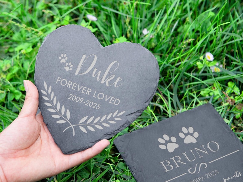 Puede incluir: Una placa conmemorativa para mascotas de pizarra en forma de coraz&oacute;n con la inscripci&oacute;n "Duke FOREVER LOVED 2009-2025" y una corona de laurel. Tambi&eacute;n se ve una placa cuadrada con "BRUNO" y huellas de patas. Ambas son de color gris oscuro.