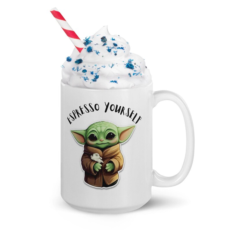 May include: White ceramic mug with a green character holding a small white creature. The mug has blue and white frosting on top and says "Espresso Yourself" in black text.