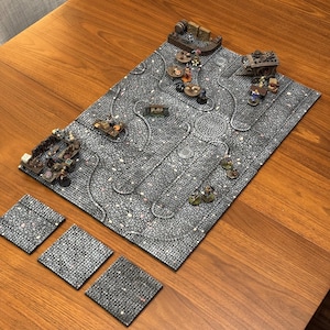 Puede incluir: Un conjunto de cuatro baldosas de textura de piedra gris para juegos de mesa. Las baldosas están dispuestas en forma de cuadrado sobre una superficie de madera. Una baldosa de textura de piedra gris más grande con un diseño de camino es visible en el fondo.
