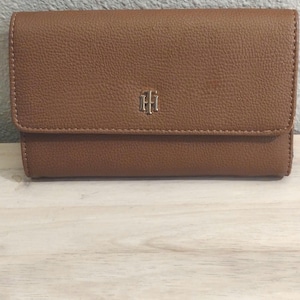 Cartera Tommy Hilfiger de piel color canela. Cierre a presión. Capacidad para 6 tarjetas y 1 DNI. Tiene espacio para el teléfono. Compartimento trasero con cremallera.
