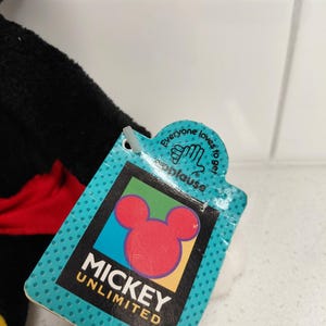 May include: A close-up of a Mickey Unlimited tag with a red Mickey Mouse head logo. The tag is teal with white polka dots and the text "Mickey Unlimited" in black. The tag also has the text "Everyone loves to get applause."