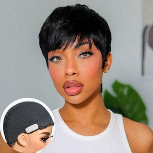 May include: A short, black pixie cut wig with textured layers and side-swept bangs. The inset shows the interior of the black wig cap, which features a soft, adjustable fabric band and a mesh construction designed for a secure and comfortable fit.