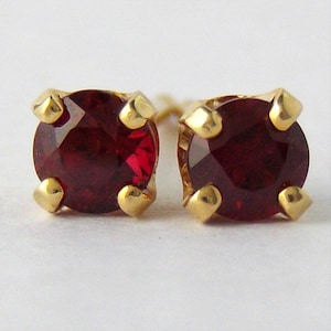 May include: A pair of gold stud earrings with red gemstones. The earrings are small and delicate.