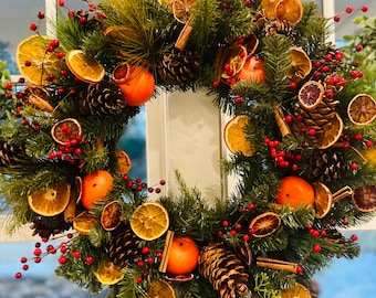 May include: A Christmas wreath made of evergreen branches decorated with dried orange slices, cinnamon sticks, pine cones, and red berries.