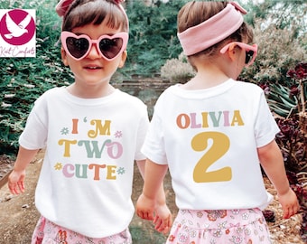 May include: Two children wearing white t-shirts with colorful text. One shirt says "I'M TWO CUTE" and the other says "OLIVIA 2". Both children wear pink heart-shaped sunglasses and headbands. The shirts are for a second birthday.