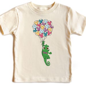 May include: A white t-shirt with a green chameleon holding onto a bunch of colorful balloons. The balloons are shaped like Mickey Mouse ears.