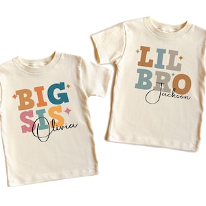 May include: Two cream colored t-shirts with colorful text. One shirt says "BIG SIS Olivia" and the other says "LIL BRO Jackson".