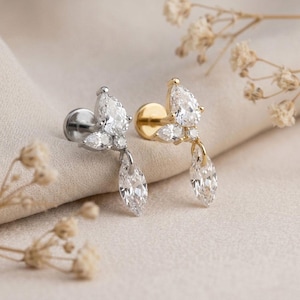 May include: Two stud earrings featuring a cluster of clear, pear-shaped and marquise-cut stones. One earring is crafted from silver-toned metal, while the other is made of gold-toned metal. Each piece includes a flat back post and a dangling stone.