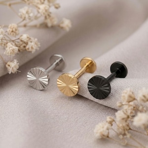 May include: Three flat-back labret studs featuring circular heads with a radial sunburst pattern. The set includes one silver-toned, one gold-toned, and one black-toned stud, each constructed with a straight post and a flat circular base for secure fit.