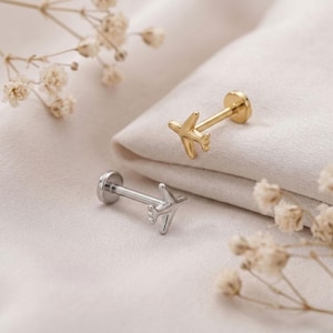 May include: Two flat back stud earrings featuring a small airplane design. One earring is finished in a polished gold tone, while the other is finished in a polished silver tone. Each stud has a straight post and a circular flat back closure.