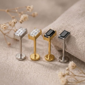 May include: Four flat-back stud earrings featuring rectangular baguette-cut stones. Two studs have clear stones set in silver and gold-toned metal, while two studs have black stones set in gold-toned and silver-toned metal, all with a post back.