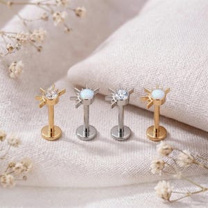 May include: Four flat-back stud earrings featuring a sunburst design. Two earrings are gold-toned with a clear crystal and an iridescent opal stone, while two are silver-toned with a clear crystal and an iridescent opal stone respectively.